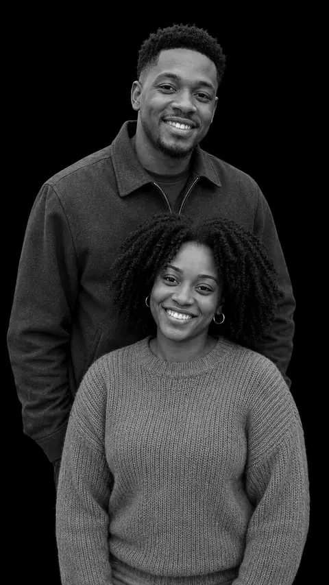 A couple in a stacked monochrome studio portrait: a man in a zip-collar jacket behind a woman with shoulder-length natural curls and hoop earrings