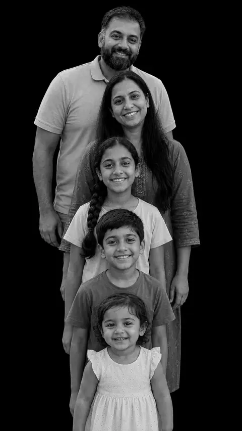 A family of five in a stacked monochrome studio portrait: a bearded man, a woman in an embroidered kurta, a girl with a long braid, a boy, and a toddler in a white dress