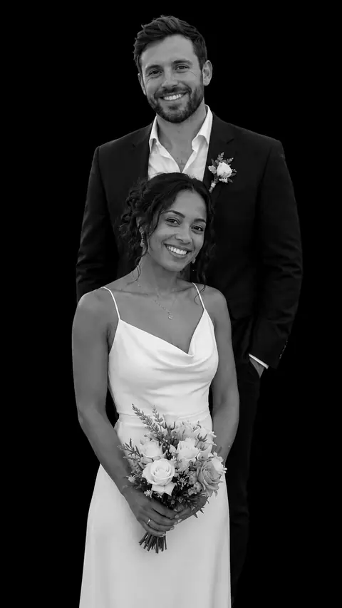A newly married couple in a stacked monochrome studio portrait: a groom in a dark suit with a boutonnière behind a bride in a satin slip dress holding a rose bouquet